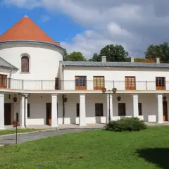 Zamek w Lesku, biały budynek z okrągłą wieżą i pomarańczowym dachem, otoczony zielenią.