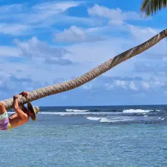 Mężczyzna w kapeluszu wisi na palmie nad turkusową wodą. Idealny dzień na plaży w Laguna Beach.