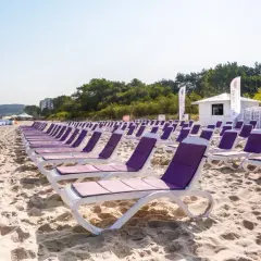 Rzędy leżaków na piaszczystej plaży, idealne na tygodniowe wczasy nad morzem z wyżywieniem. W tle morze i zieleń.