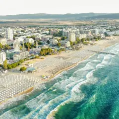 Słoneczne bułgaria plaże z rzędami leżaków i parasoli, turkusowe morze i nadmorskie miasto w tle.