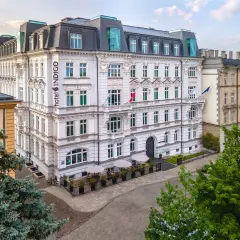 Hotel Indigo, idealny na city break z Warszawy. Elegancka fasada, ogródek z parasolami i zielone drzewa tworzą przytulną atmosferę.