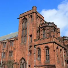 Imponująca, ceglana architektura w stylu gotyckim w Manchesterze, z charakterystycznymi wieżyczkami i łukowymi oknami.