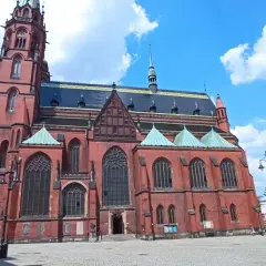 Gotycka katedra w mieście nad Kaczawą, z ceglaną fasadą i zielonymi dachami, na tle błękitnego nieba z chmurami.