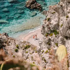 Malownicze kalabryjskie plaże z turkusową wodą i skalistymi klifami. Dwie osoby odpoczywają na piaszczystej plaży, ciesząc się słońcem.