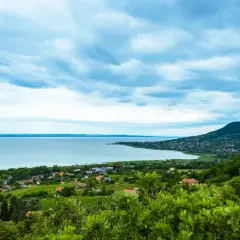 Widok na jezioro Balaton z zielonymi wzgórzami i domkami. Chmury na niebie tworzą dramatyczny krajobraz.