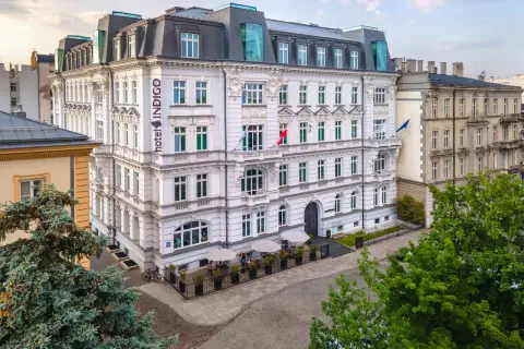 Hotel Indigo, idealny na city break z Warszawy. Elegancka fasada, ogródek z parasolami i zielone drzewa tworzą przytulną atmosferę.