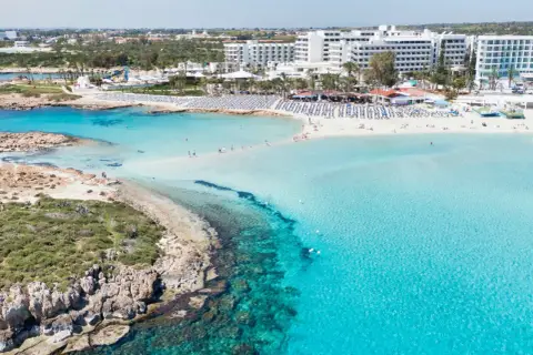 Piękna plaża na Cyprze z turkusową wodą i hotelami. Sprawdź aktualne cypr ceny wakacji!