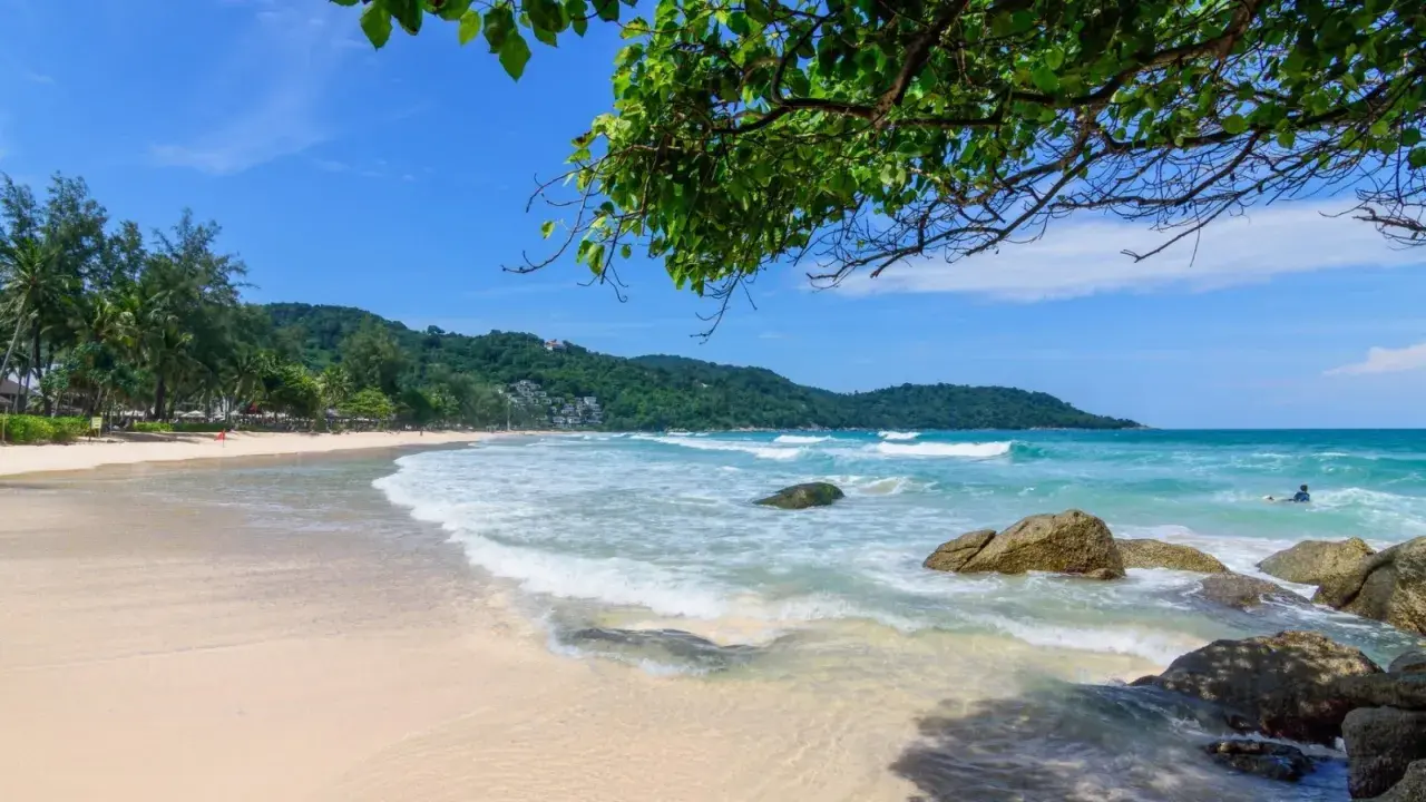 Piękna plaża Kata Beach z turkusową wodą, falami i zielonymi wzgórzami w tle.