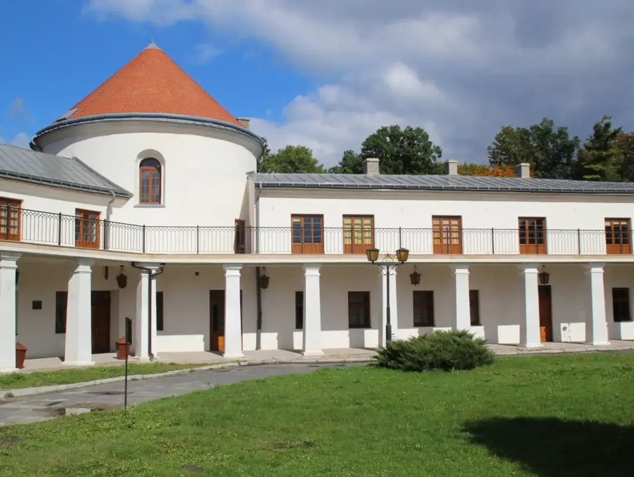 Zamek w Lesku, biały budynek z okrągłą wieżą i pomarańczowym dachem, otoczony zielenią.