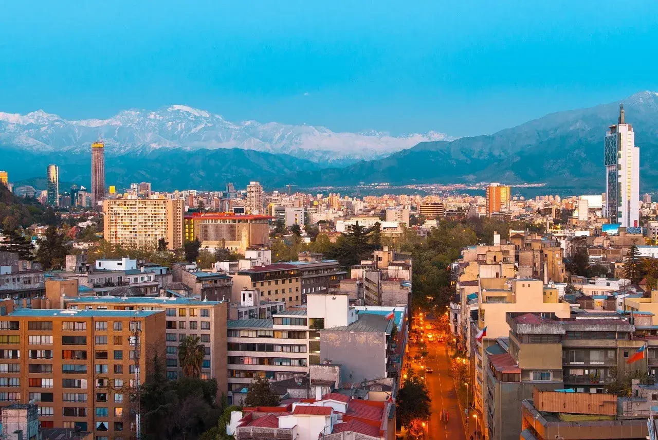 Widok na Santiago, stolicę Chile, z górami w tle. Miasto tętni życiem, a światła uliczne rozświetlają wieczór.