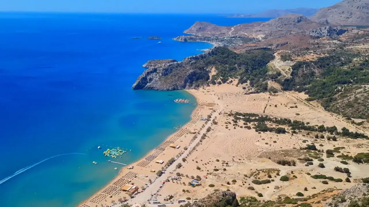 Malownicze plaże Rodos z turkusową wodą, leżakami i wodnym parkiem rozrywki. Widok z góry na wybrzeże i górzysty krajobraz.