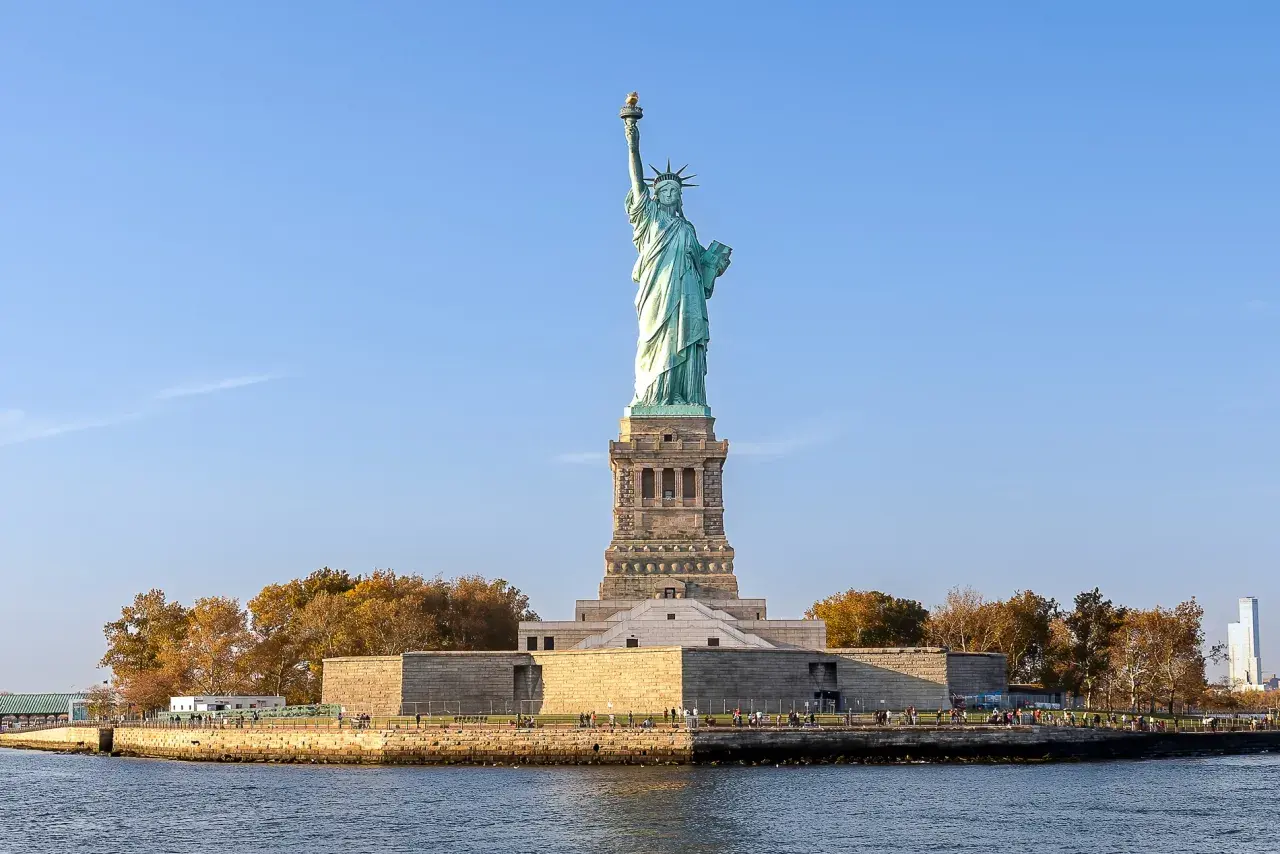 Gdzie jest Statua Wolności? Na wyspie Liberty Island w Nowym Jorku, dumnie wznosi się symbol wolności, otoczona wodą i jesiennymi drzewami.
