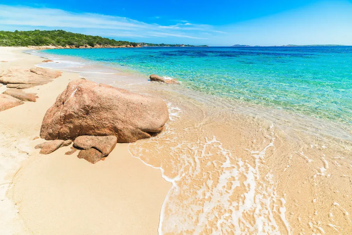 Piękna plaża na Costa Smeralda, Sardynia, z turkusową wodą, złotym piaskiem i skalistym wybrzeżem.