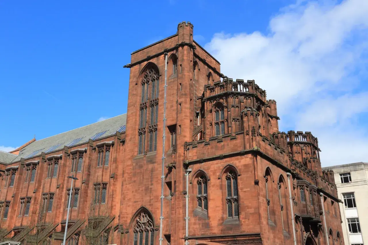 Imponująca, ceglana architektura w stylu gotyckim w Manchesterze, z charakterystycznymi wieżyczkami i łukowymi oknami.