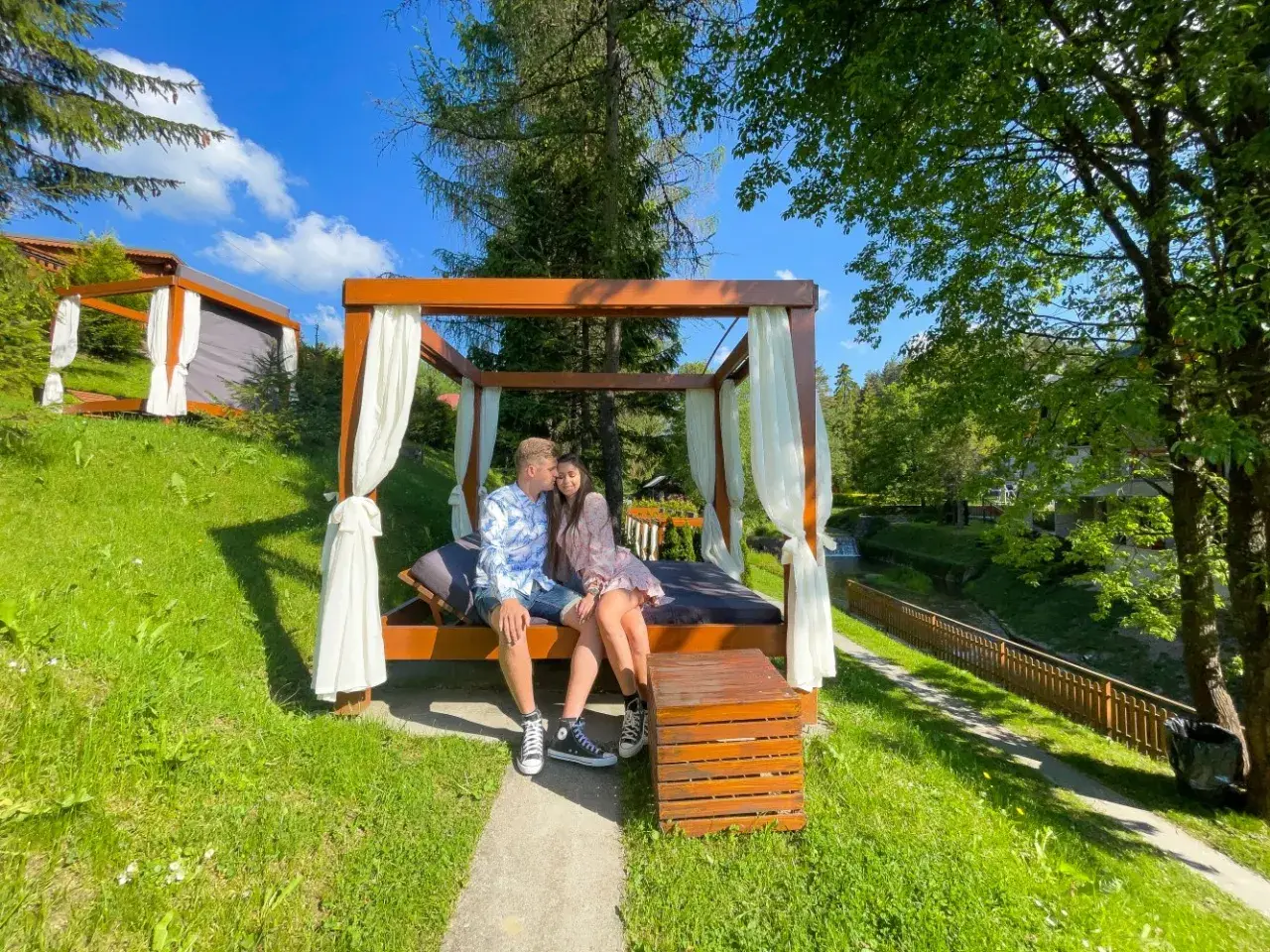 Idealne miejsce, gdzie na weekend we dwoje. Para odpoczywa na łóżku pod baldachimem w otoczeniu zieleni i strumyka.
