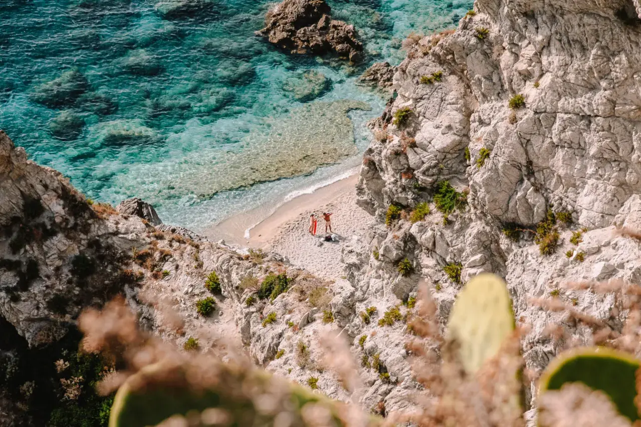 Malownicze kalabryjskie plaże z turkusową wodą i skalistymi klifami. Dwie osoby odpoczywają na piaszczystej plaży, ciesząc się słońcem.
