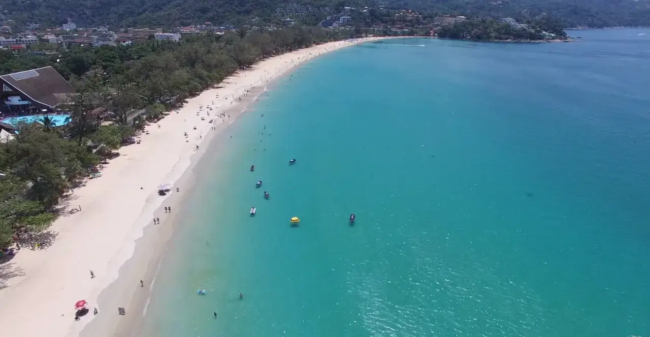 Słoneczny dzień na plaży Kata, z turkusową wodą i białym piaskiem, pełen ludzi i wodnych atrakcji.