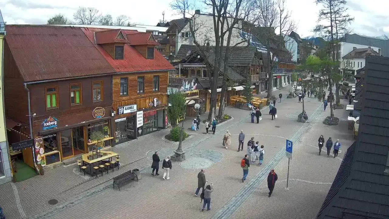 Spacer po Krupówkach w Zakopanem. Ludzie przechadzają się wśród drewnianych budynków, sklepów i restauracji.