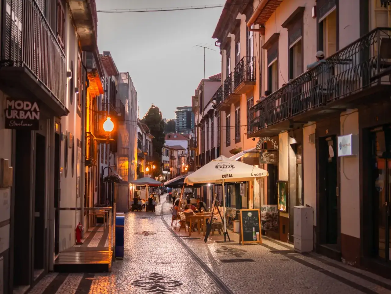 Ulica w Funchal, stolicy Madery, wieczorem. Widać restauracje z ogródkami, sklepy i brukowaną ulicę.