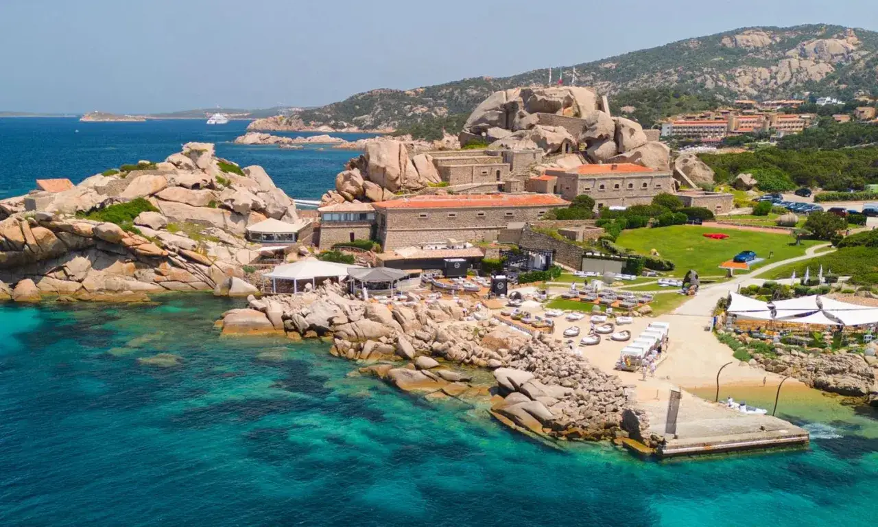 Wyjątkowe widoki na Costa Smeralda Sardynia: turkusowe morze, skaliste wybrzeże i luksusowy kurort z białymi parasolami i leżakami.