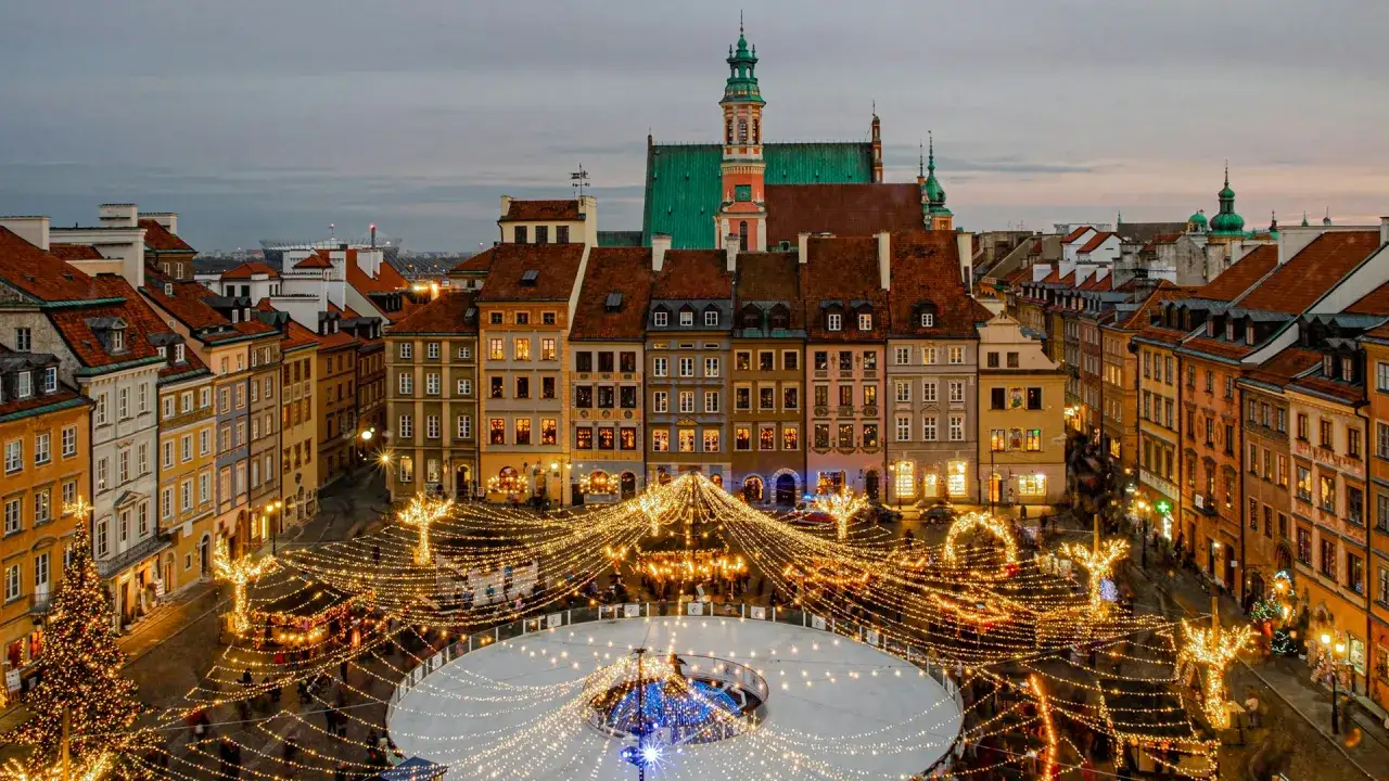 Oświetlony jarmark bożonarodzeniowy na Rynku Starego Miasta w Warszawie. Lodowisko, choinka i kolorowe kamienice tworzą magiczną atmosferę idealną na city break z Warszawy.