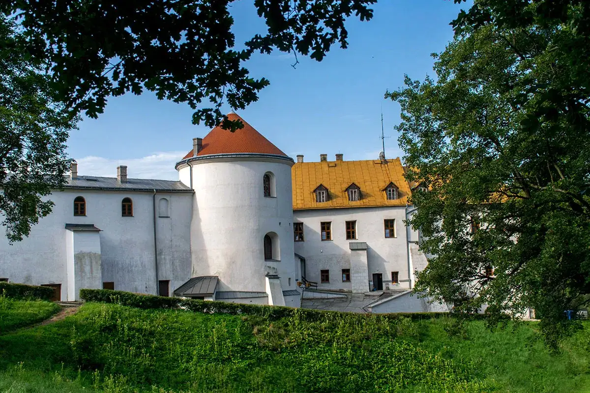 Zamek w Lesku, biała twierdza z okrągłą wieżą i pomarańczowym dachem, otoczona zielenią.